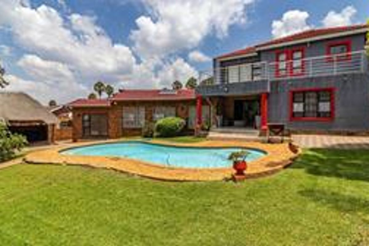Rear view of the property featuring a swimming pool, paved patio area, and a detached thatched lapa in the garden.