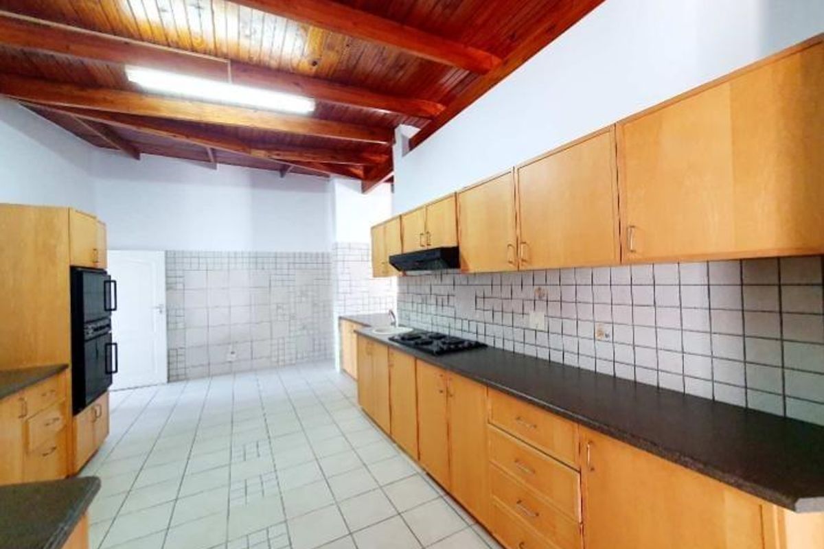 Spacious kitchen featuring wooden cabinetry, built-in oven, gas hob, extractor fan, and tiled flooring under a high exposed timber beam ceiling.