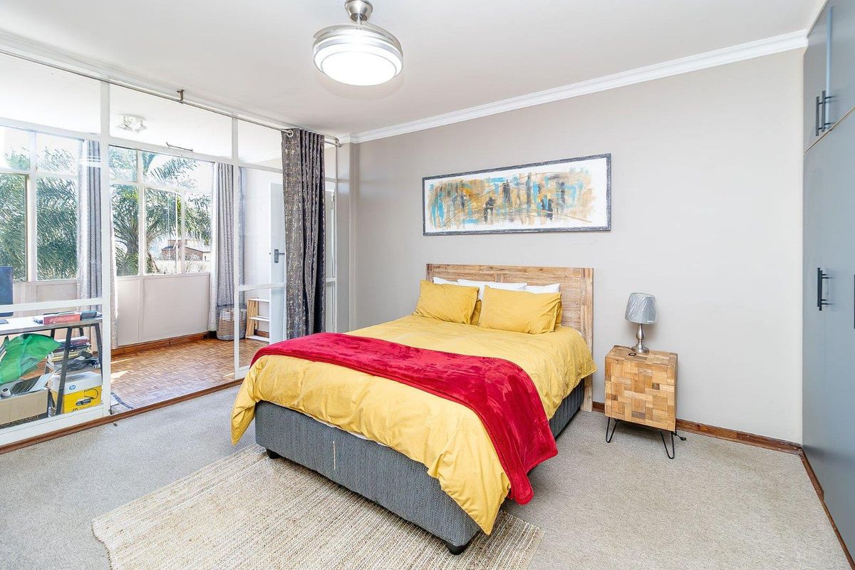 A well-lit bedroom featuring neutral walls, carpeted flooring, a built-in wardrobe, and direct access to an enclosed balcony through sliding glass doors.