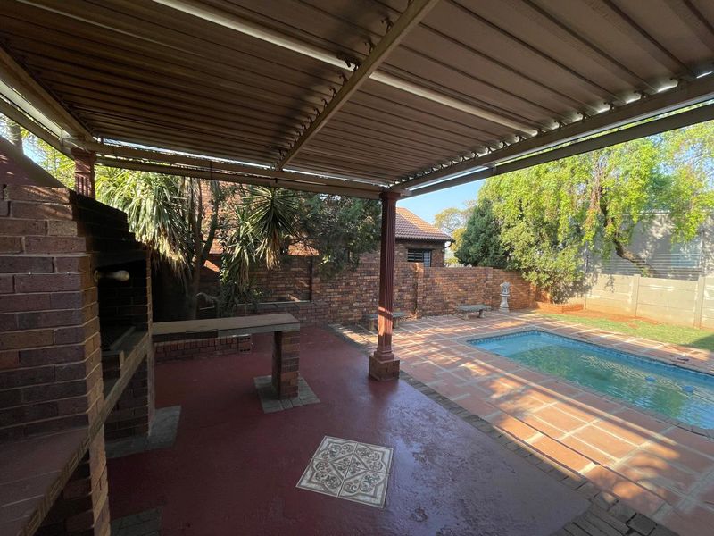 Covered outdoor patio featuring a built-in brick braai, overlooking a private swimming pool and garden area.