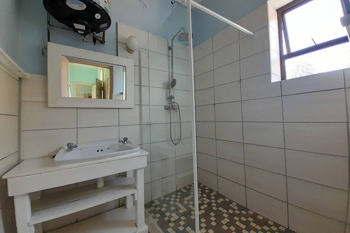 A functional bathroom featuring a walk-in shower with glass screen, wall-mounted basin, and an exposed electric water heater unit.