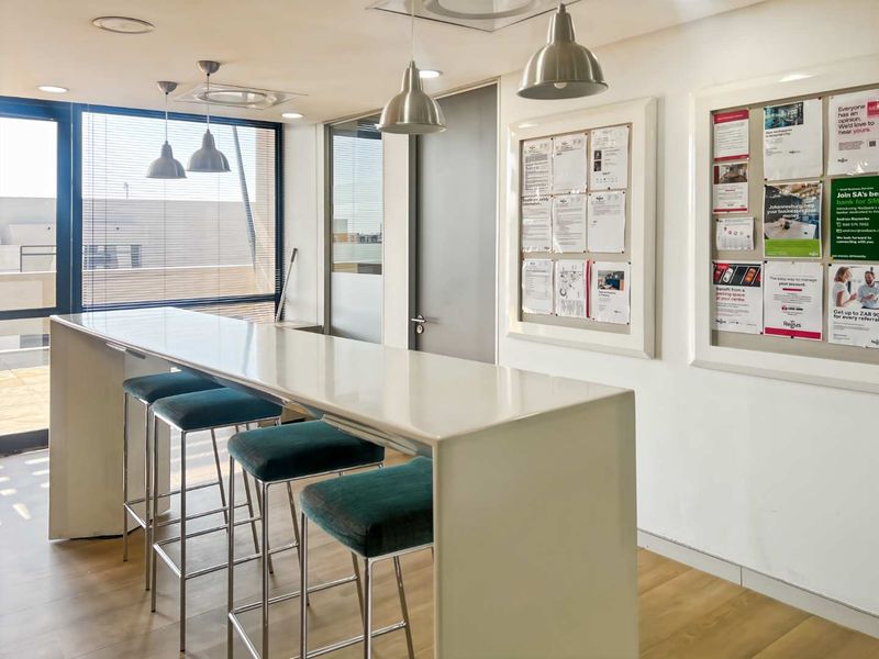 A modern office break-out area featuring a sleek built-in breakfast bar, pendant lighting, and laminate flooring, creating a functional and professional workspace environment.