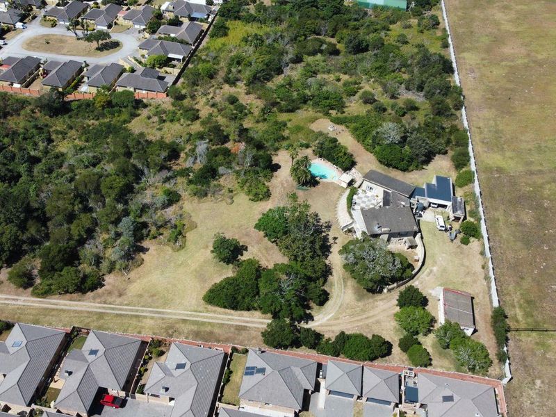 Aerial view of a residential property featuring a swimming pool, established garden, and outbuildings set within a large, partially cleared plot.