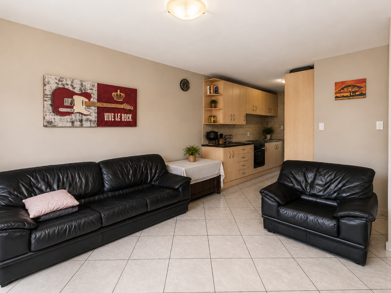 Open-plan living area featuring a functional kitchen with built-in cabinetry, oven, and hob, complemented by neutral tiled flooring throughout the space.