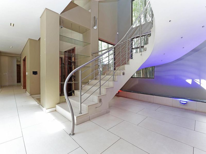 Spacious entrance hall featuring a striking curved staircase with stainless steel balustrade, modern tiled flooring, and integrated accent lighting.