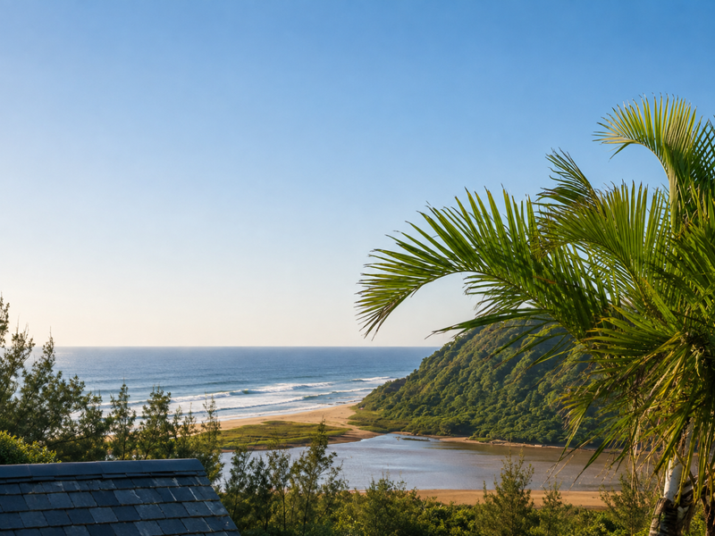 A scenic elevated view overlooking the coastline, featuring a river estuary, sandy beach, and lush green hills.