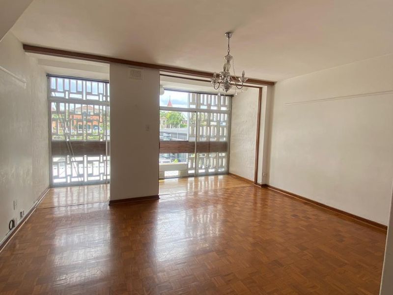 Spacious living area featuring original parquet flooring, decorative metal window screens, and a staircase, offering a bright and open layout.