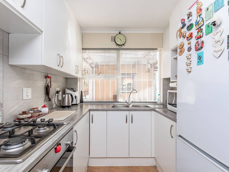 Compact kitchen featuring white cabinetry, laminate countertops, a gas hob, built-in oven, and a stainless steel sink with natural light from the window.