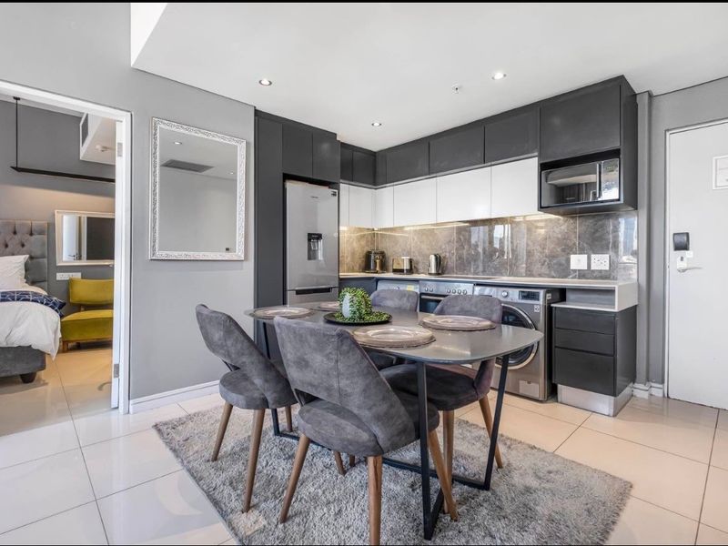 Modern open-plan kitchen and dining area featuring sleek two-tone cabinetry, stone countertops, and integrated appliances, with tiled flooring throughout.