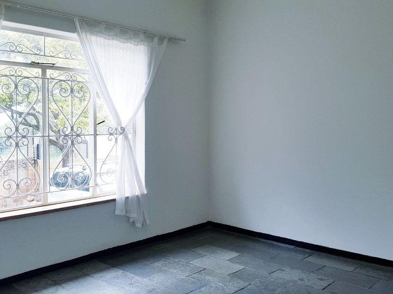 A bright, empty bedroom featuring stone tile flooring and a window with decorative security bars.