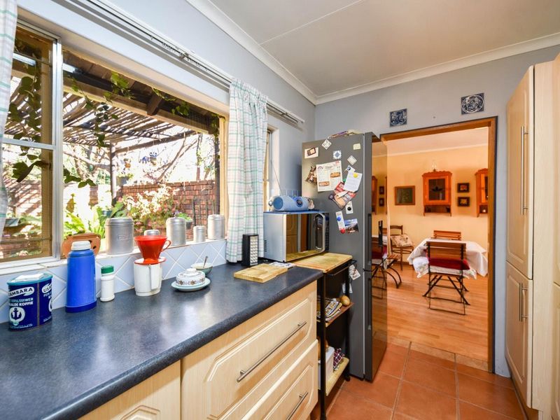 A functional kitchen featuring laminate cabinetry, dark countertops, and tiled flooring, with a view through to the adjacent dining area.