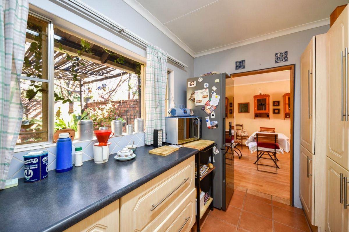 A functional kitchen featuring laminate cabinetry, dark countertops, and tiled flooring, with a view through to the adjacent dining area.