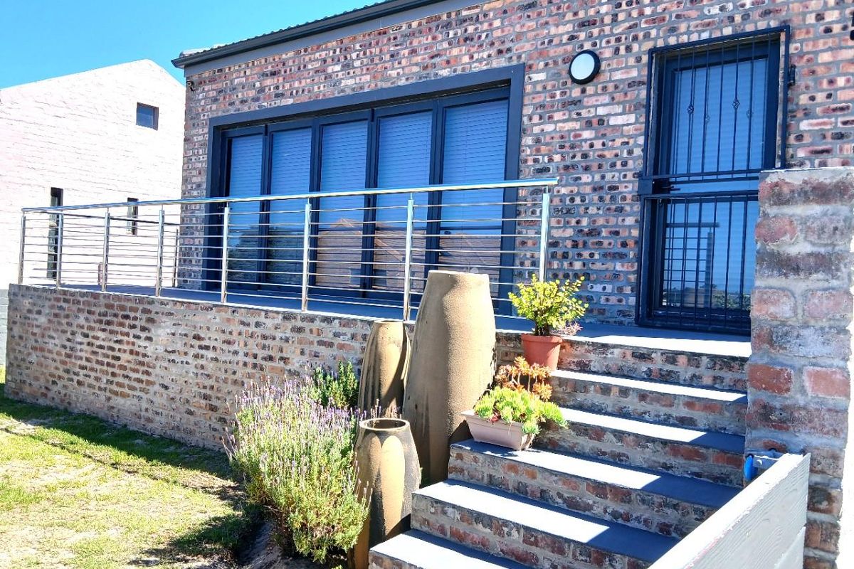 A rear exterior view featuring a face-brick facade, a raised patio with stainless steel balustrades, and concrete steps leading to the entrance.