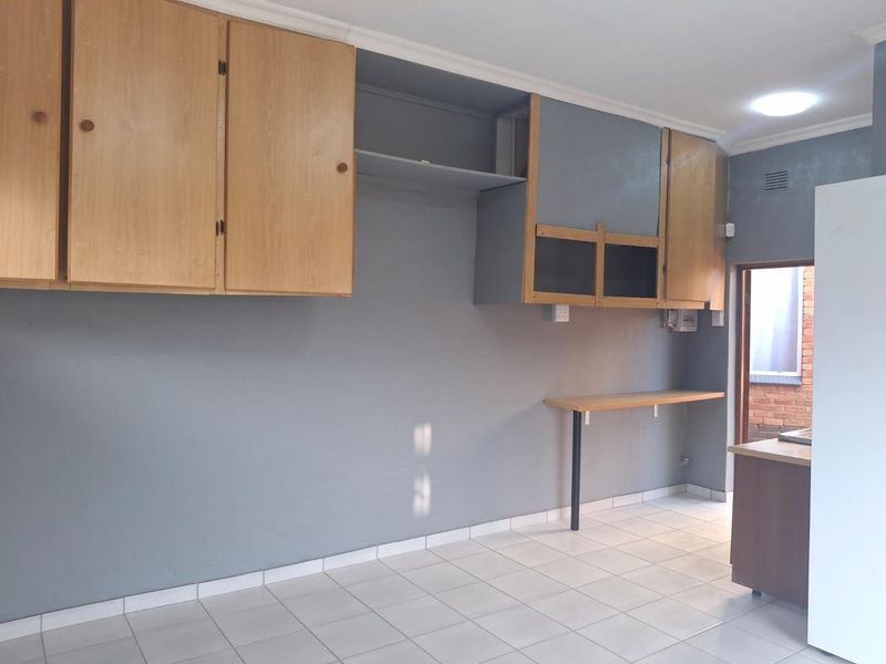 An empty kitchen area featuring tiled flooring, wall-mounted cabinetry, and a fixed breakfast bar, offering a blank canvas for renovation.
