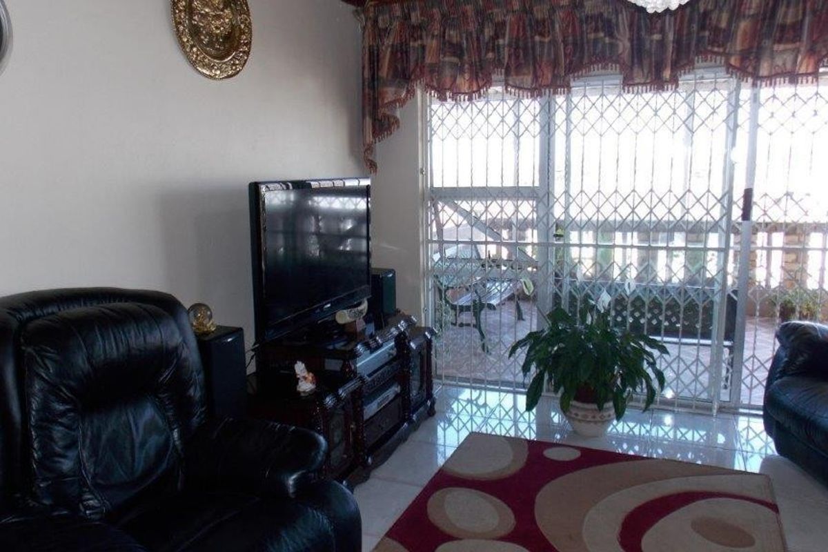 A living room featuring tiled flooring and a sliding glass door with integrated security gate, providing access to an outdoor patio area.