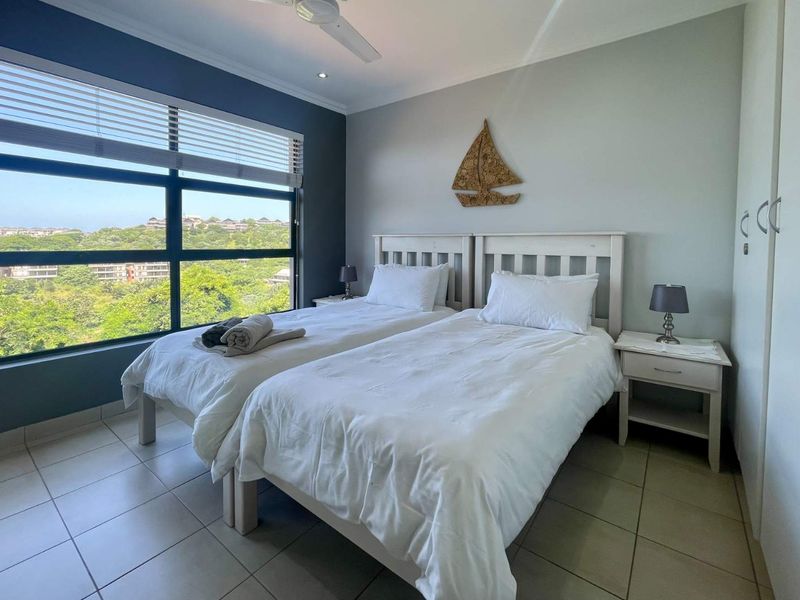 A bright bedroom featuring large windows with scenic views, tiled flooring, built-in cupboards, and a ceiling fan.