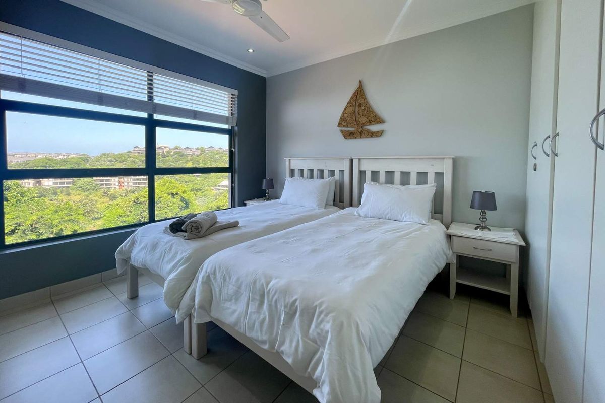 A bright bedroom featuring large windows with scenic views, tiled flooring, built-in cupboards, and a ceiling fan.