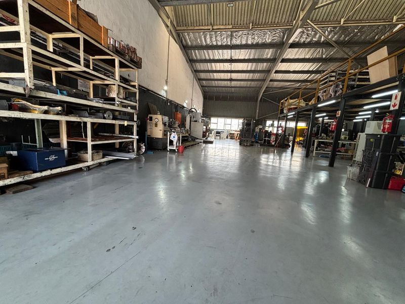 Spacious industrial warehouse featuring high ceilings with exposed steel trusses, durable epoxy flooring, and a functional mezzanine level for additional storage or workspace.