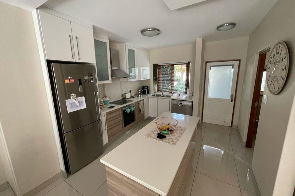 Modern kitchen featuring a central island, built-in cabinetry, stainless steel appliances, and tiled flooring, offering a functional and well-lit workspace.