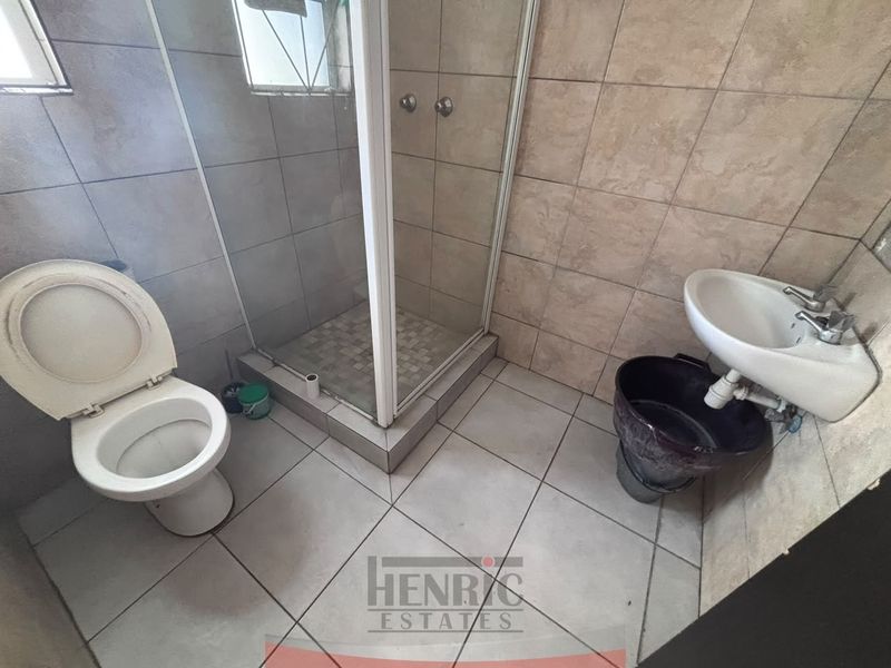 A compact bathroom featuring a shower enclosure, toilet, and wall-mounted basin with tiled finishes throughout, requiring cosmetic updates.