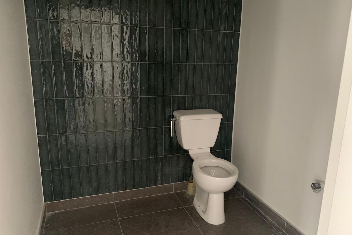 A modern bathroom featuring dark vertical wall tiles, large format floor tiles, and a standard white toilet suite.