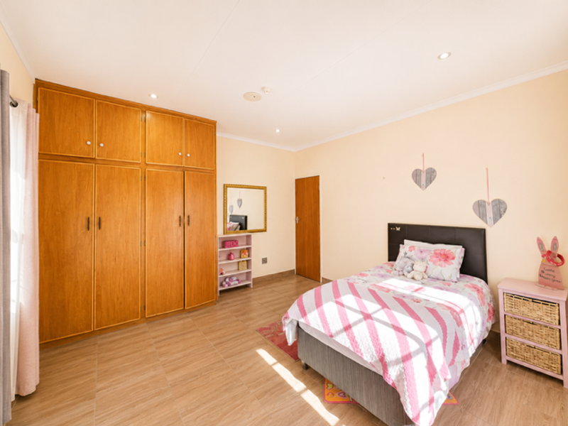 A well-maintained bedroom featuring extensive built-in wooden cabinetry, tiled flooring, and recessed downlighting, offering a clean and functional living space.