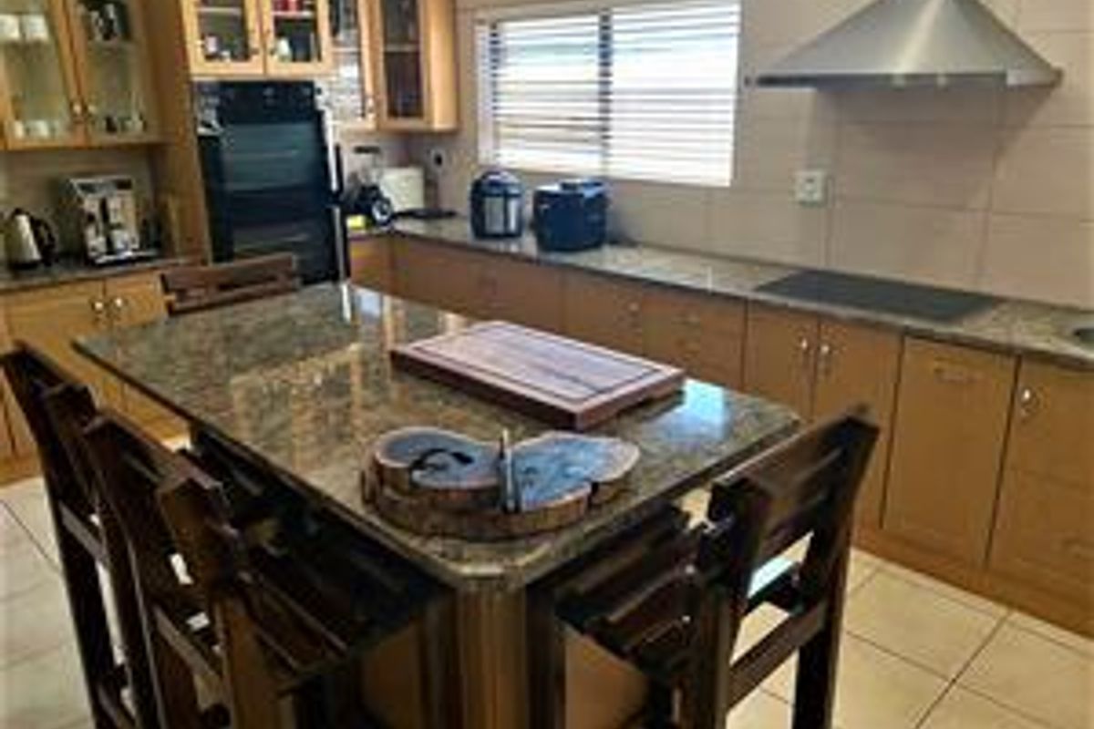 A functional kitchen featuring wooden cabinetry, granite countertops, a central island, and built-in appliances including an oven and extractor fan.