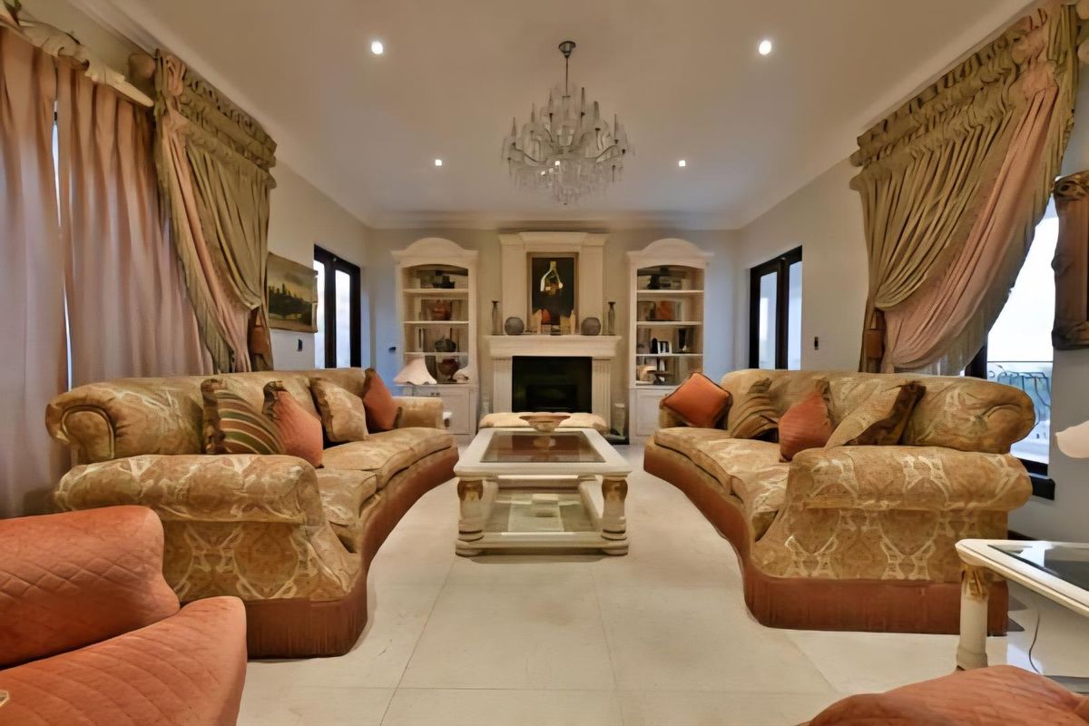 A formal living room featuring a central fireplace with built-in shelving units, recessed ceiling lighting, and a decorative crystal chandelier.
