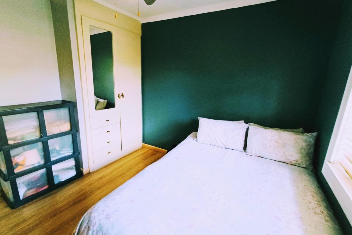 A bedroom featuring built-in cabinetry with integrated mirror, wood-look flooring, and a dark accent wall.