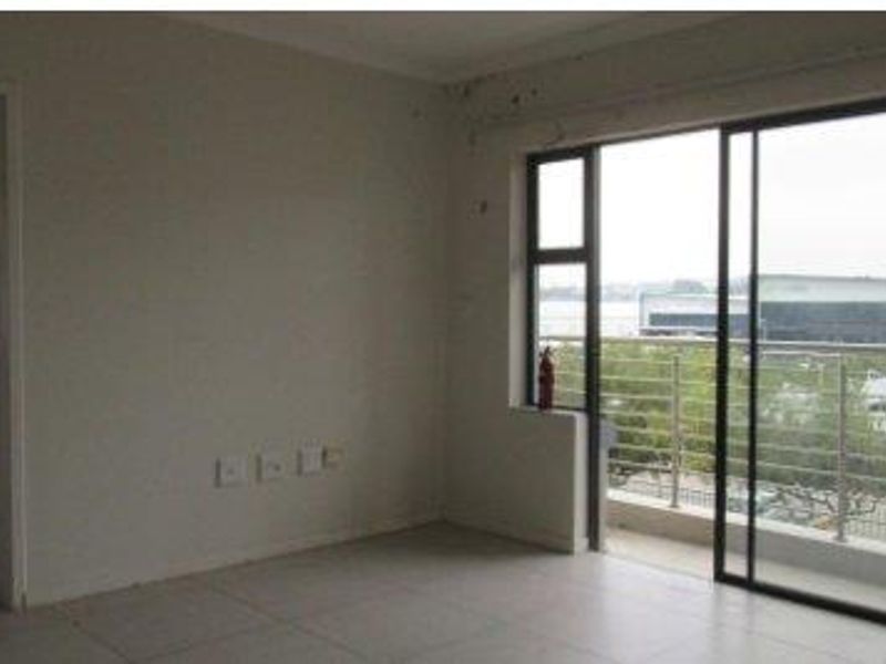 An empty living room featuring tiled flooring and a large sliding glass door providing access to a balcony with exterior views.