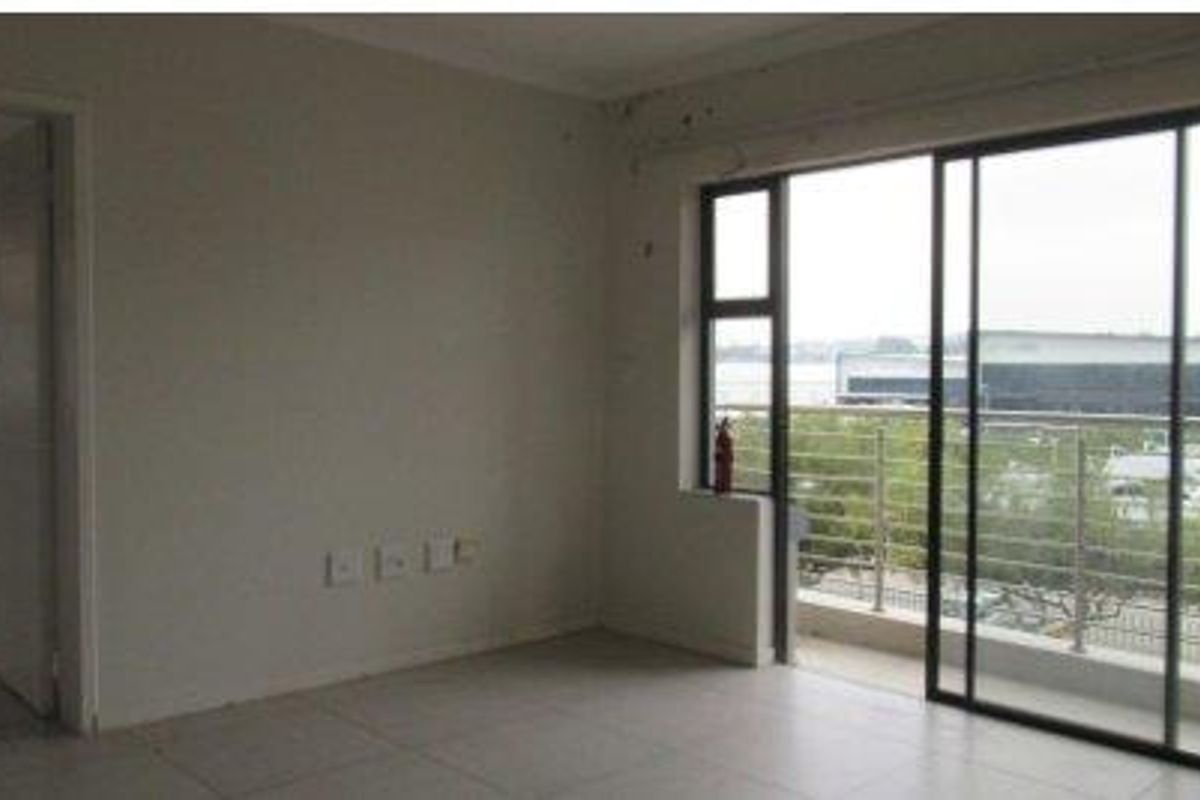 An empty living room featuring tiled flooring and a large sliding glass door providing access to a balcony with exterior views.