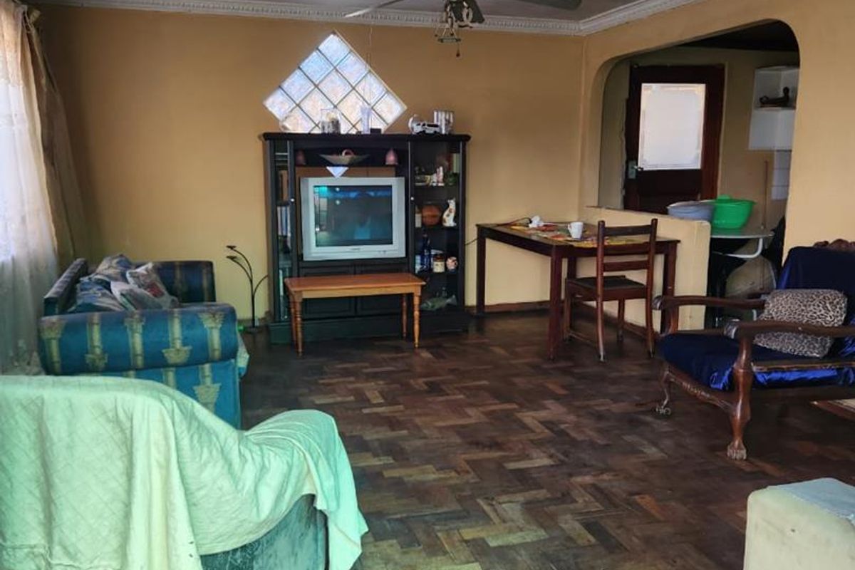 A living room featuring traditional parquet flooring, a ceiling fan with a decorative rose, and a diamond-shaped glass block window.
