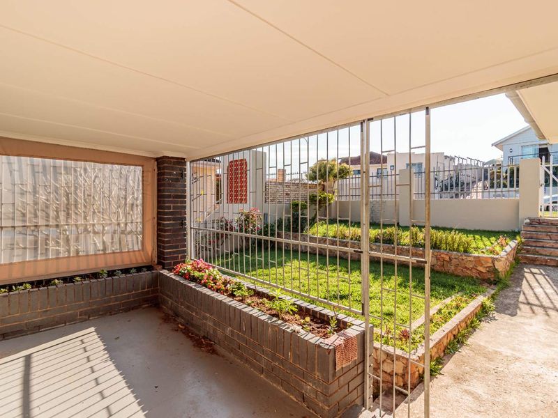 A covered patio area featuring built-in brick planter boxes and secure metal gating, overlooking a small private garden space.