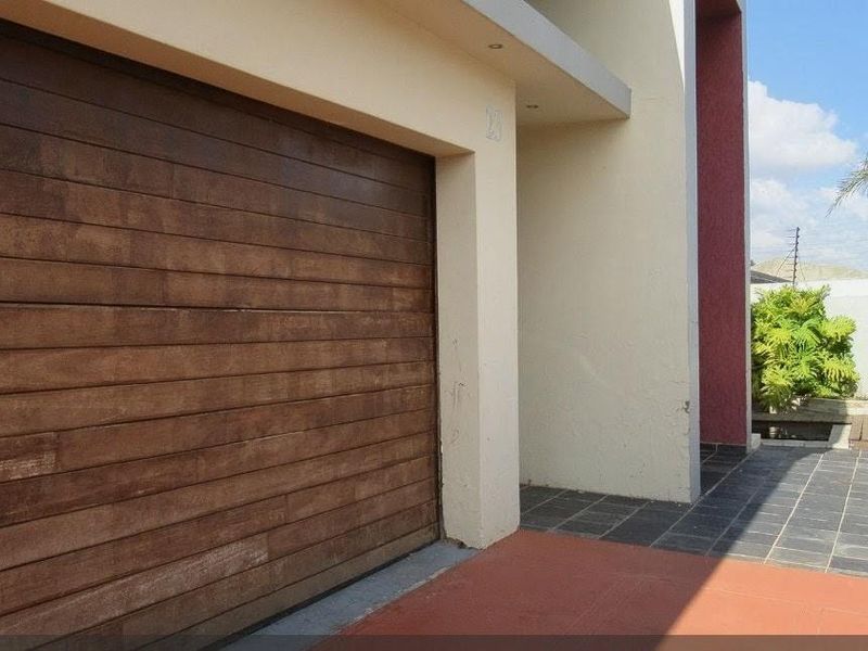 Front elevation of the property featuring a wooden sectional garage door, tiled driveway, and plastered exterior walls with perimeter electric fencing.