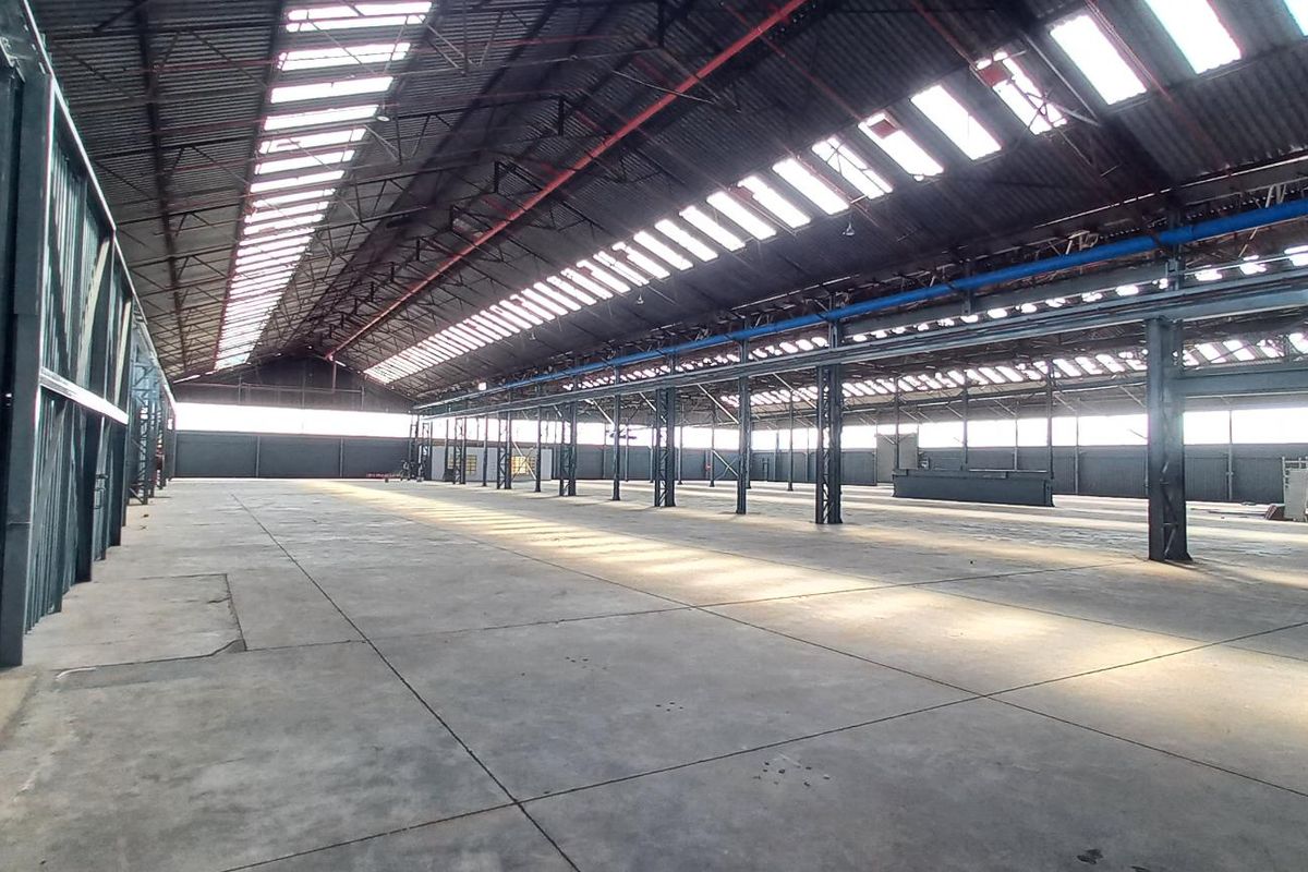 Expansive industrial warehouse space featuring a high-clearance steel portal frame, concrete flooring, and natural light provided by extensive roof skylights.
