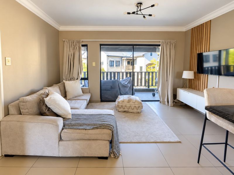 A bright and modern living room featuring tiled floors, a timber slat feature wall, and large sliding doors leading to a private balcony.