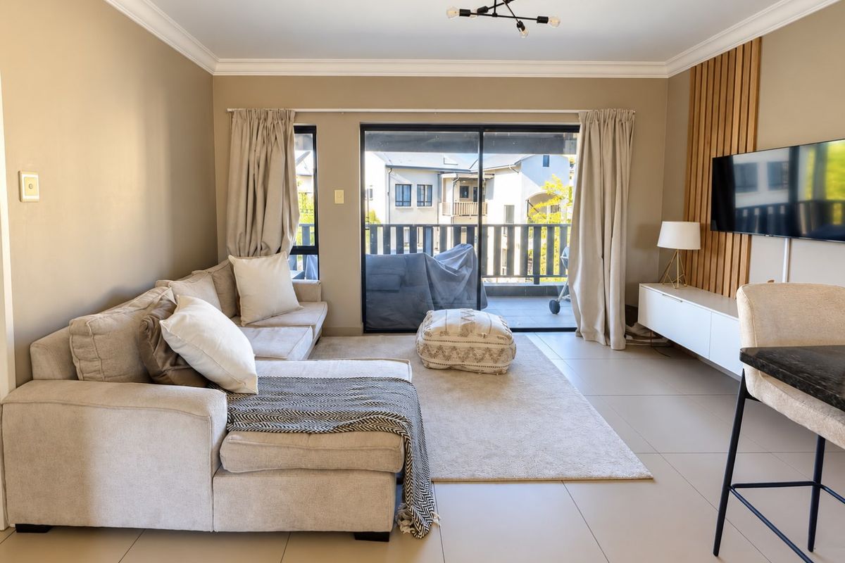 A bright and modern living room featuring tiled floors, a timber slat feature wall, and large sliding doors leading to a private balcony.