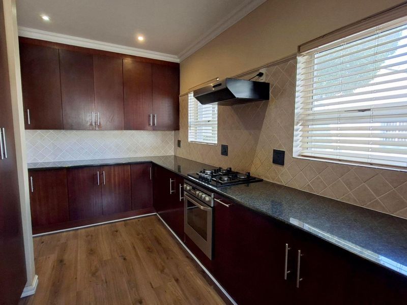 A well-maintained kitchen featuring dark wood cabinetry, granite countertops, a built-in oven, gas hob, and extractor fan with neutral tiled backsplash.