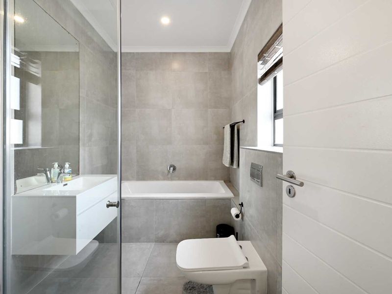 Modern bathroom featuring a wall-mounted vanity, built-in bathtub, wall-hung toilet, and a glass-enclosed shower with neutral floor-to-ceiling tiling.