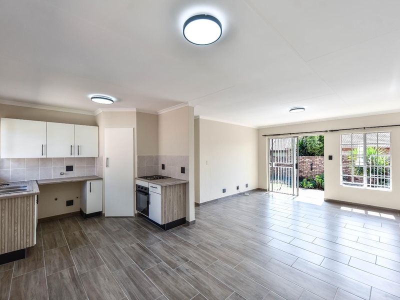 Spacious open-plan living area featuring a functional kitchen with built-in cabinetry, oven, and hob, leading directly to an outdoor patio area.