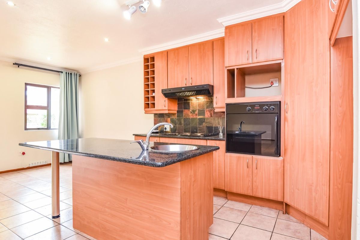 A functional kitchen featuring wood-look cabinetry, a granite-topped island with a prep sink, built-in oven, and tiled flooring.
