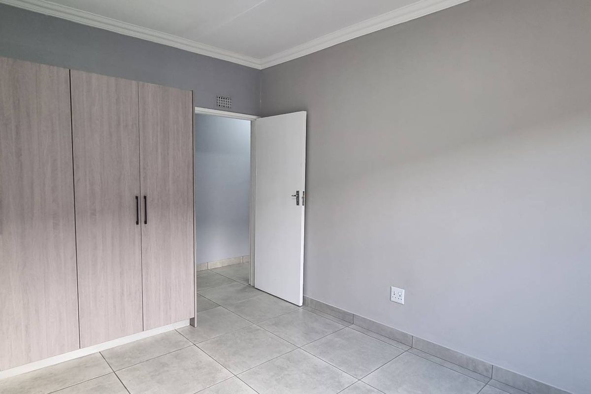 A clean, modern bedroom featuring neutral grey walls, large format floor tiles, and built-in wooden cabinetry with contemporary black handles.