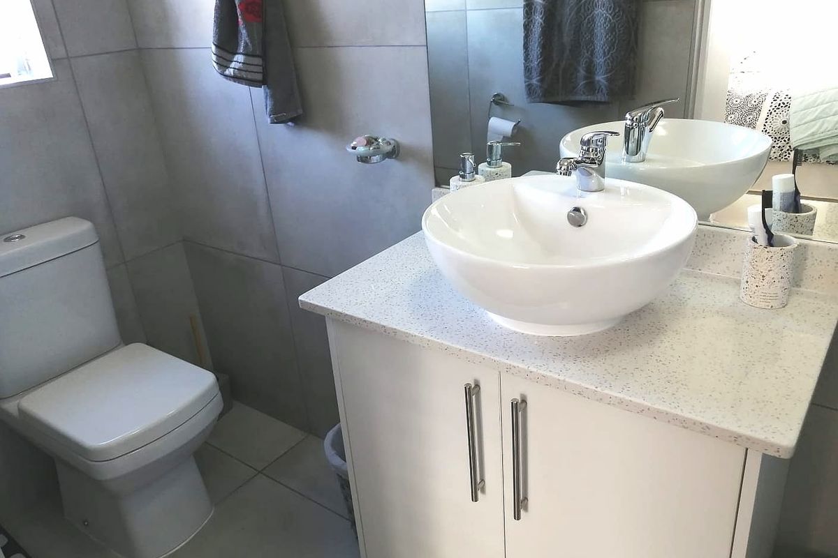 Modern bathroom featuring a white vessel sink on a stone-look vanity, a dual-flush toilet, and large format grey wall tiles.