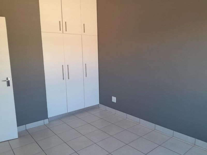 A clean, empty bedroom featuring neutral grey walls, white built-in cupboards, and light-colored floor tiles.