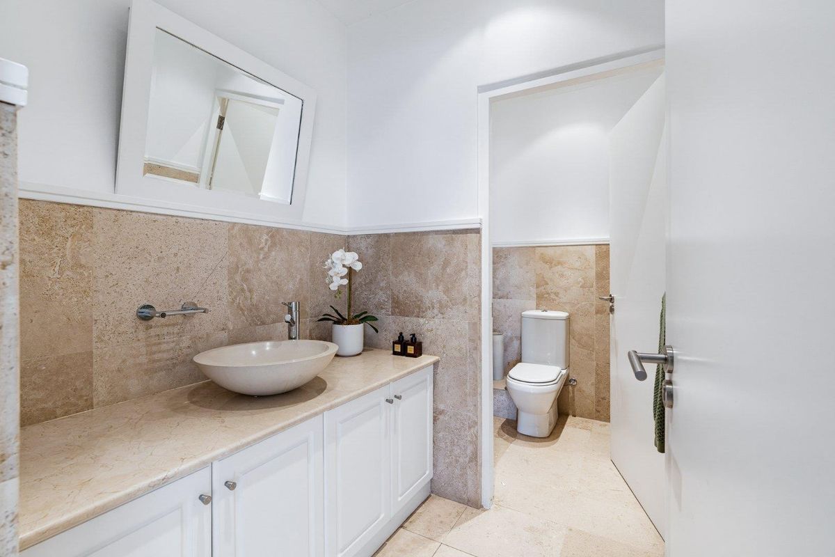 A well-maintained bathroom featuring a stone vanity with a vessel sink, stone wall and floor tiles, and a separate toilet area.