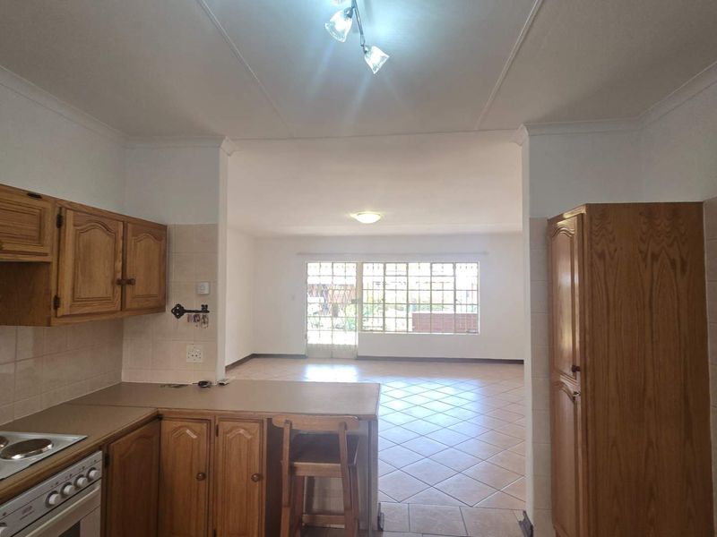 Open plan kitchen and living area featuring wooden cabinetry, tiled flooring, and direct access to the exterior through a security gate.