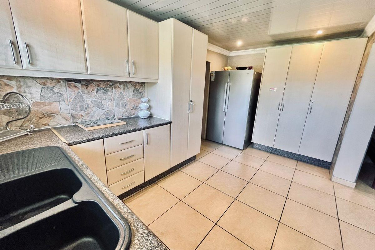 A functional kitchen featuring built-in cabinetry, stone-look countertops, a double basin sink, and tiled flooring with ample storage space.