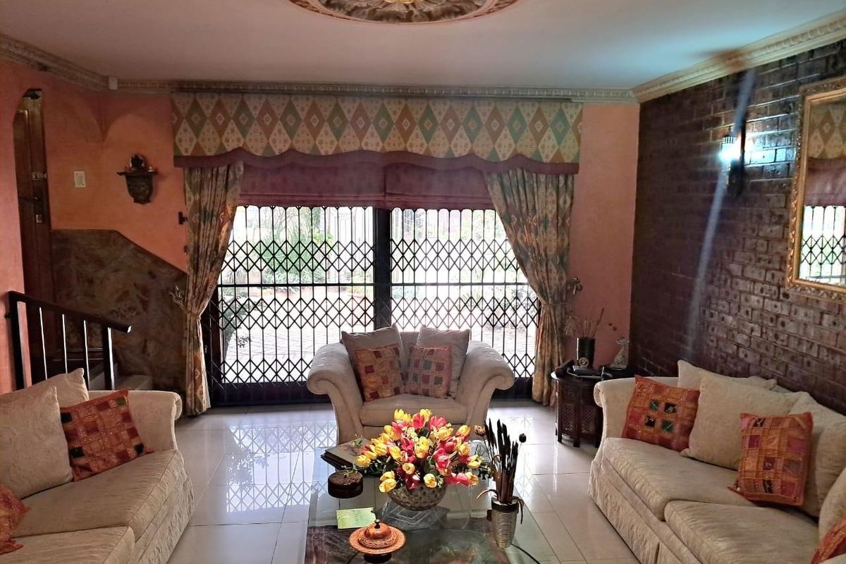 A living room featuring tiled flooring, an exposed brick feature wall, a decorative ceiling rose, and a security gate leading to the exterior.