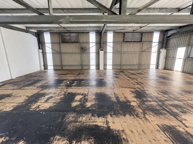A large, open-plan industrial utility space featuring exposed steel roof trusses, corrugated metal walls, and worn plywood flooring.