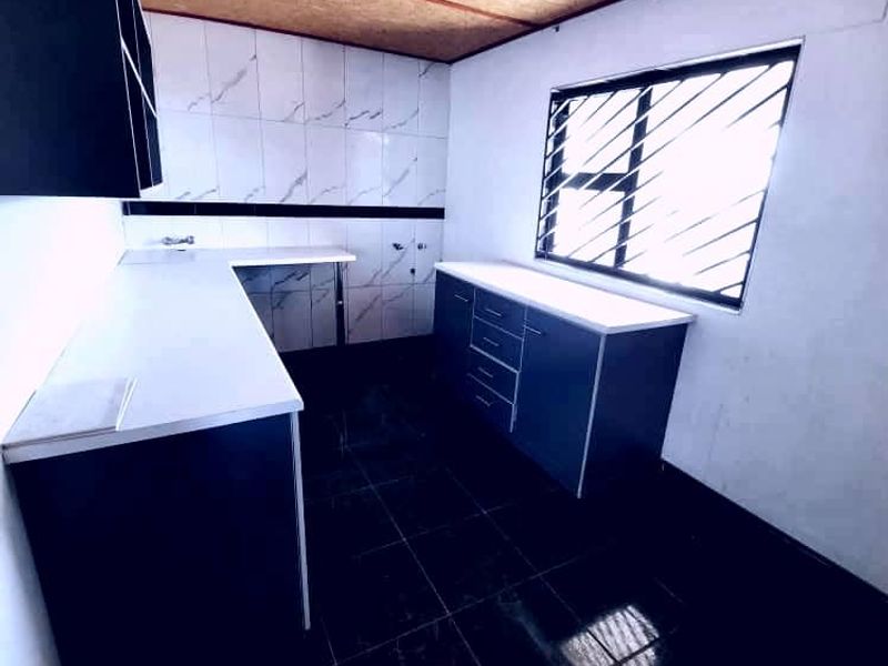 A functional kitchen space featuring dark cabinetry, white countertops, tiled backsplash, and dark floor tiles, illuminated by a central ceiling light.